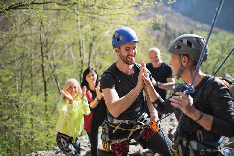 Man in blue helmet preparing for zip line adventure with guide and spectators in mountain setting
