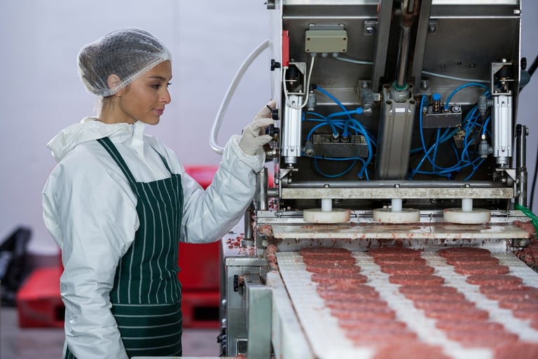 Factory worker in protective gear monitoring meat processing on industrial conveyor belt