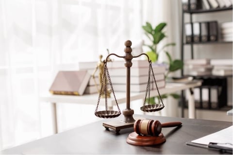 Scales of justice and wooden gavel on a desk in a law office with bookshelves in the background