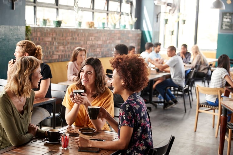 Group of people eating and socializing together at tables in a bright, casual indoor dining space with brick walls
