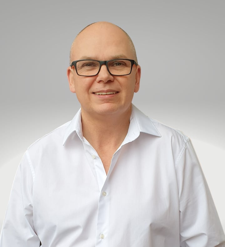 Professional headshot of Mark Woodcock wearing glasses and a white button-up shirt